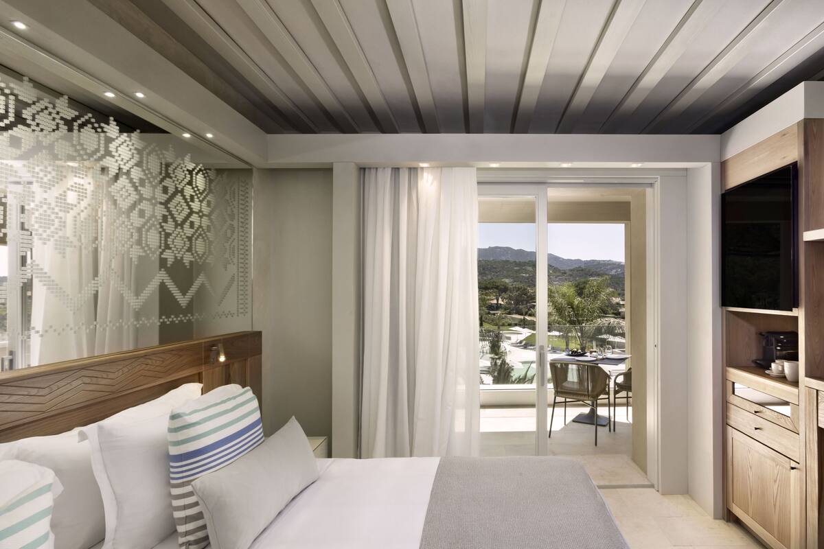 Une chambre d’hôtel moderne équipée d’un lit, d’une télévision et d’un balcon offrant une vue sur les montagnes.