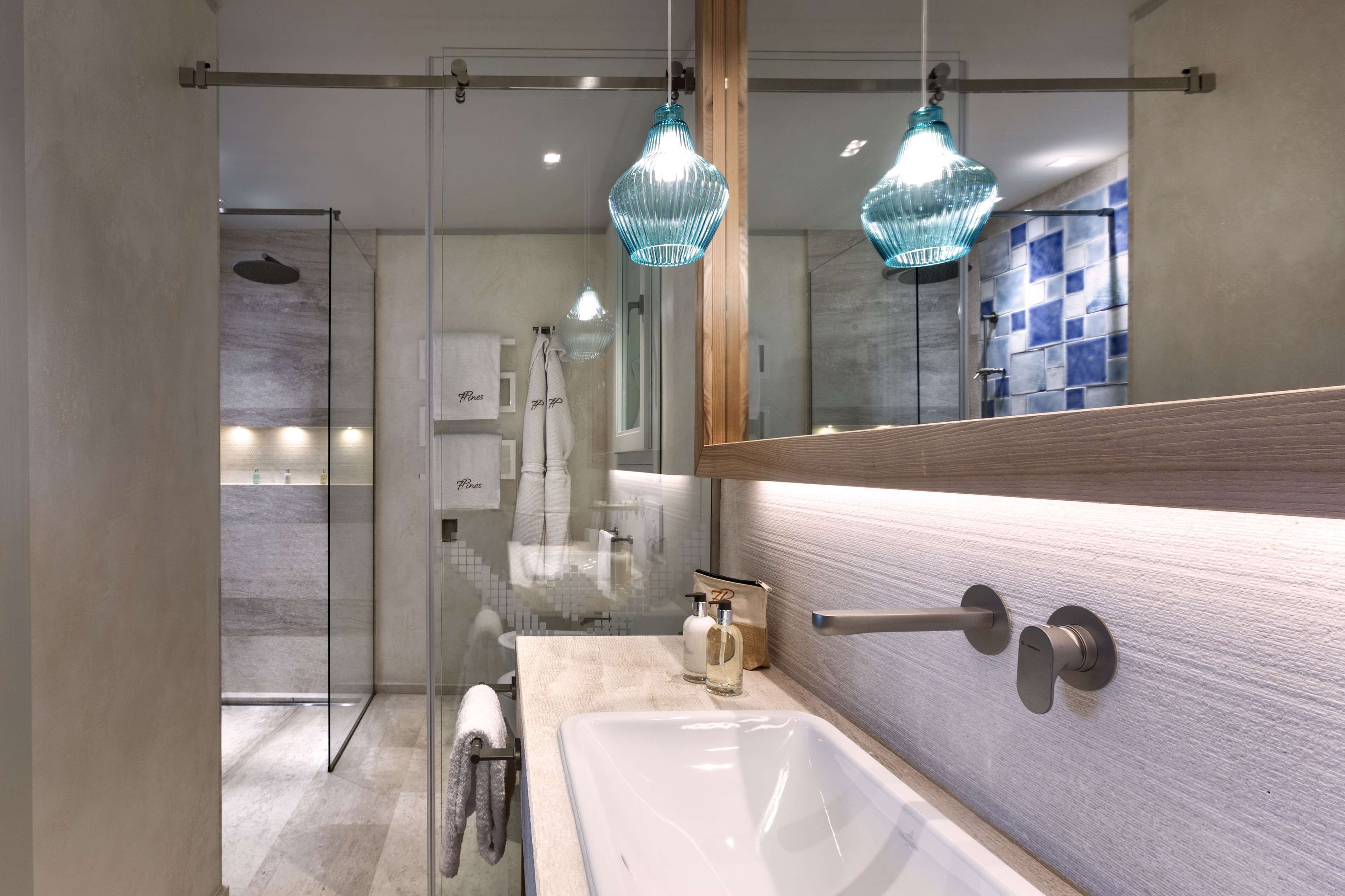 Un baño moderno con ducha acristalada, un espejo grande y lámparas colgantes.
