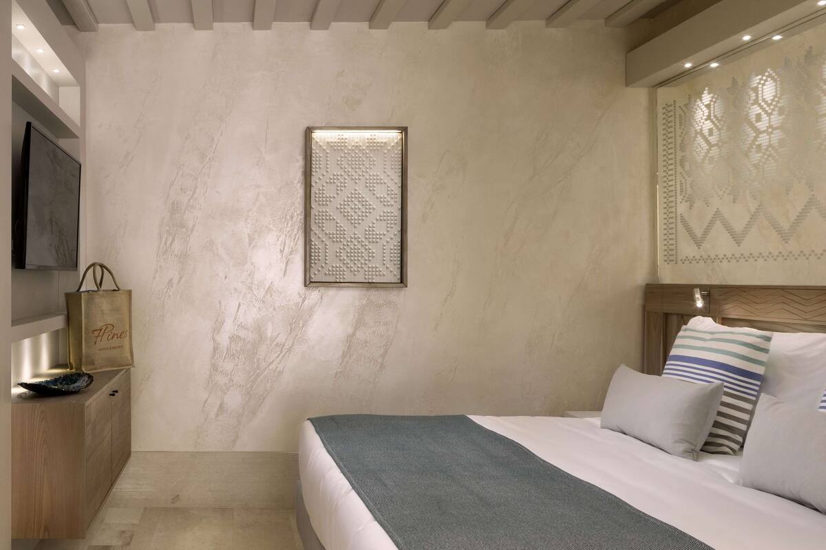 Une chambre à coucher comprenant un lit, des oreillers, une table de chevet, un téléviseur fixé au mur et un élément décoratif mural.