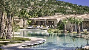 Un espace piscine agrémenté de chaises longues, de palmiers et offrant une vue sur les montagnes en arrière-plan.
