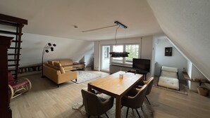Un loft spacieux avec un plafond haut, une table à manger en bois, un canapé et un téléviseur.