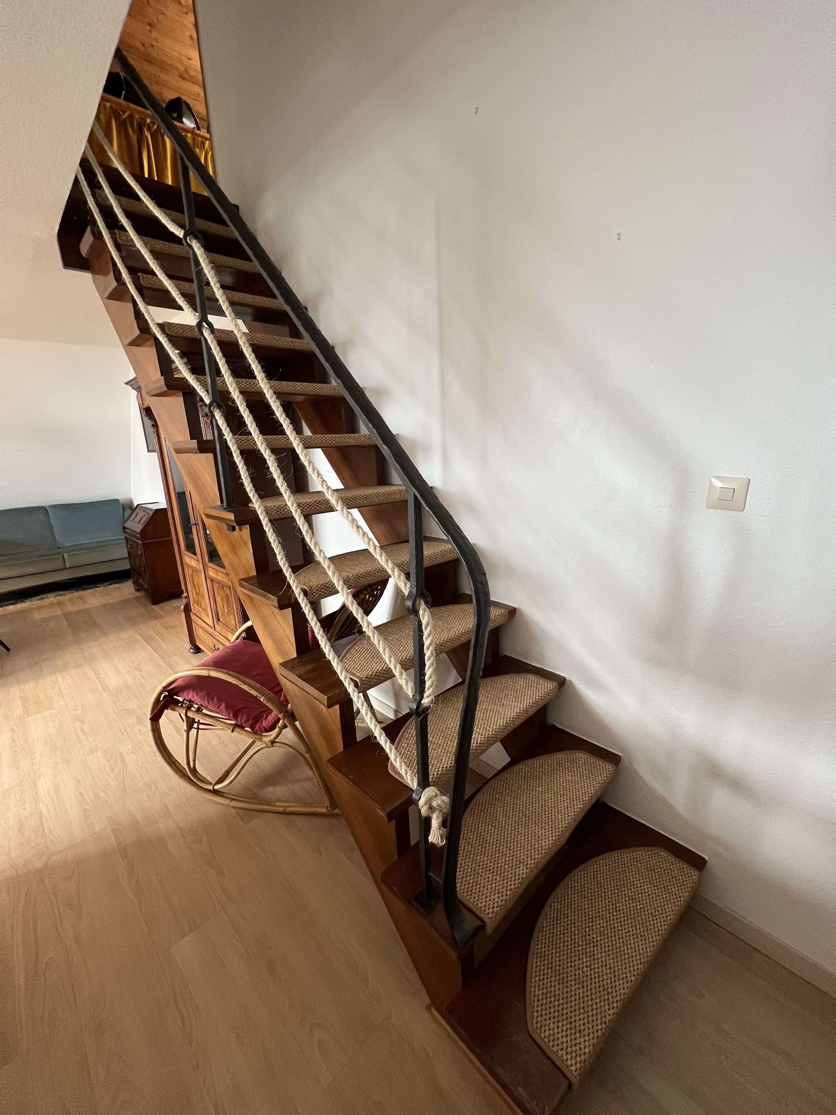 Una escalera de madera con barandilla de metal, un sillón mecedor de mimbre y un aparador de madera.