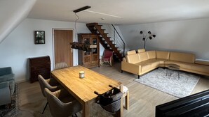 Un vaste espace de vie comprenant une table à manger en bois, un canapé beige et un escalier menant à un niveau supérieur.