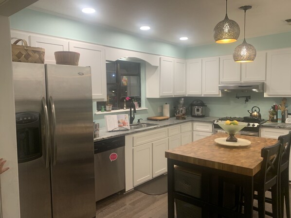 A modern kitchen with white cabinets, stainless steel appliances, and a wooden dining table.