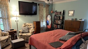 Une chambre à coucher comprenant un lit, une chaise, une bibliothèque, un téléviseur et une lampe.