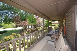 A covered porch with a view of a landscaped garden and a house in the background.
