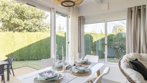 Un comedor con una mesa dispuesta para cuatro personas, ventanas amplias y una silla de mimbre.