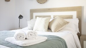 Una cama bien hecha con toallas blancas enrolladas, una colcha verde y varias almohadas.
