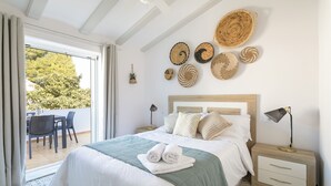 Un dormitorio con cama, mesita de noche, lámpara, cesta en la pared y vista a un patio exterior.