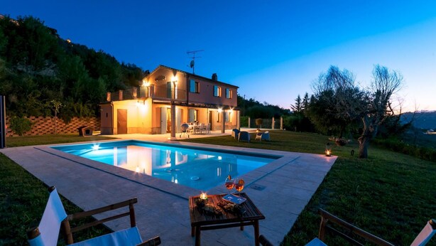 Ein zweistöckiges Haus mit Swimmingpool, Außenbereich zum Sitzen und einer gut beleuchteten Terrasse.