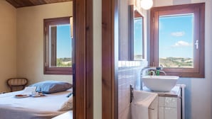 Ein Schlafzimmer mit Bett, Nachttisch mit Lampe und Fenster mit Blick auf die Landschaft.