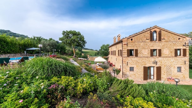 A stone building with a garden, a pool, and a clear sky.
