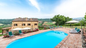 Zona de piscina con un edificio de piedra, mobiliario exterior y vistas al campo.