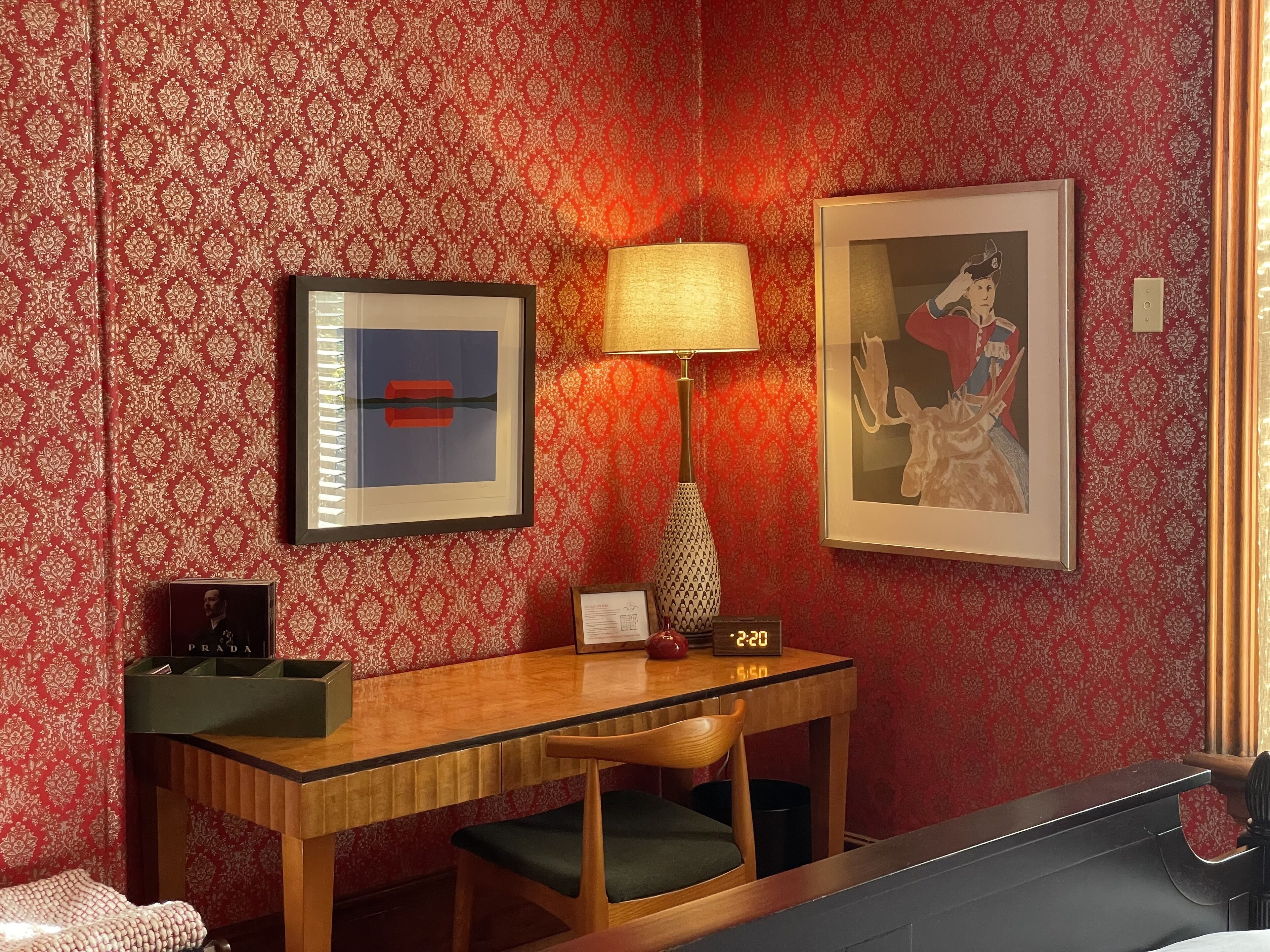 Une chambre d’hôtel avec un bureau en bois, un tableau encadré, une lampe et une horloge.