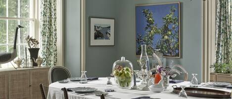 Une salle à manger avec une table dressée pour quatre personnes, un lustre et une fenêtre avec des rideaux.