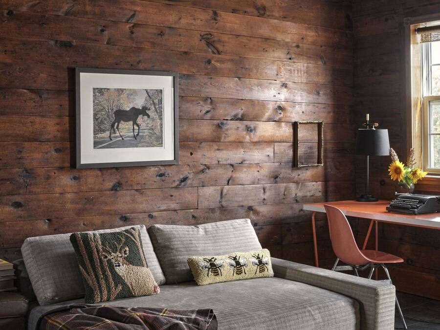 Una camera accogliente con parete in legno, un quadro incorniciato, una scrivania con una lampada e un divano comodo.