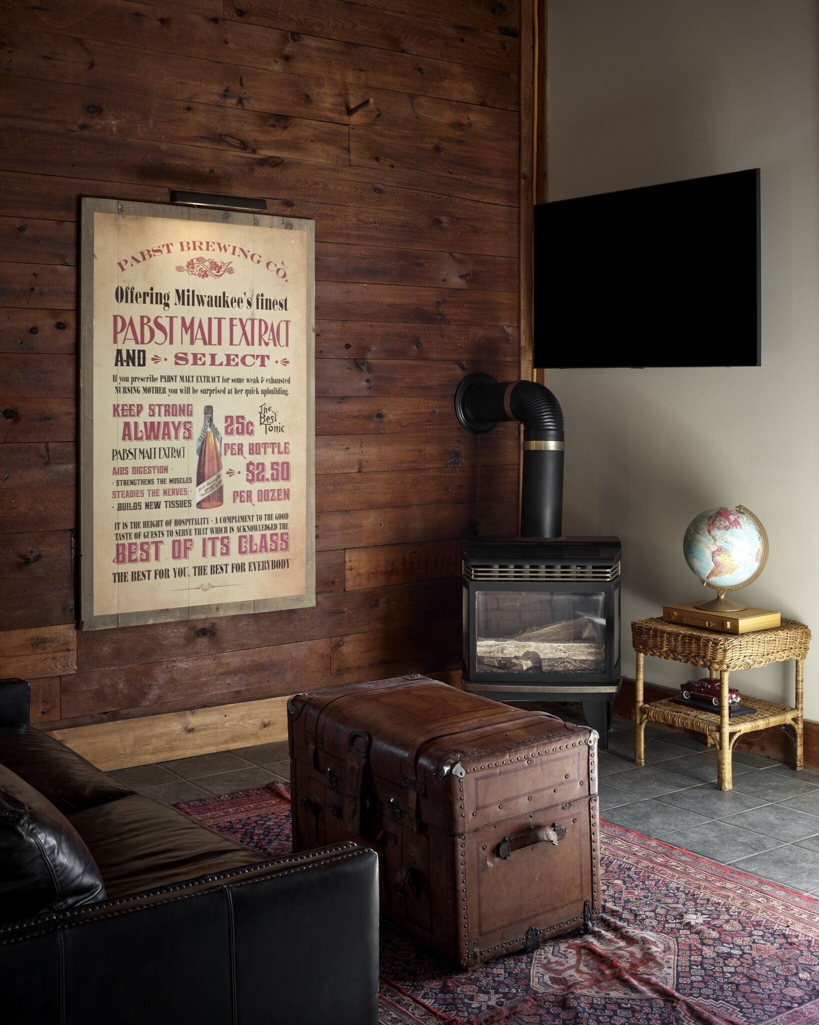 Una habitación con una pared de madera, una estufa de estilo vintage, un globo en una pequeña mesa y una maleta en el suelo.