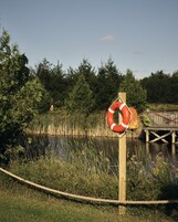 Un flotador de madera sujeto a una cuerda cerca de una masa de agua, con un puente de madera al fondo.