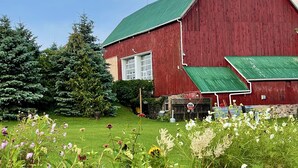 A red barn with a green roof, surrounded by lush greenery and flowering plants. - The Eddie Hotel and Farm (Prince Edward)