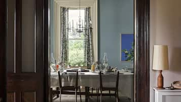 A dining room with a wooden door leading to a dining table set for four, a chandelier, and a view of greenery outside.