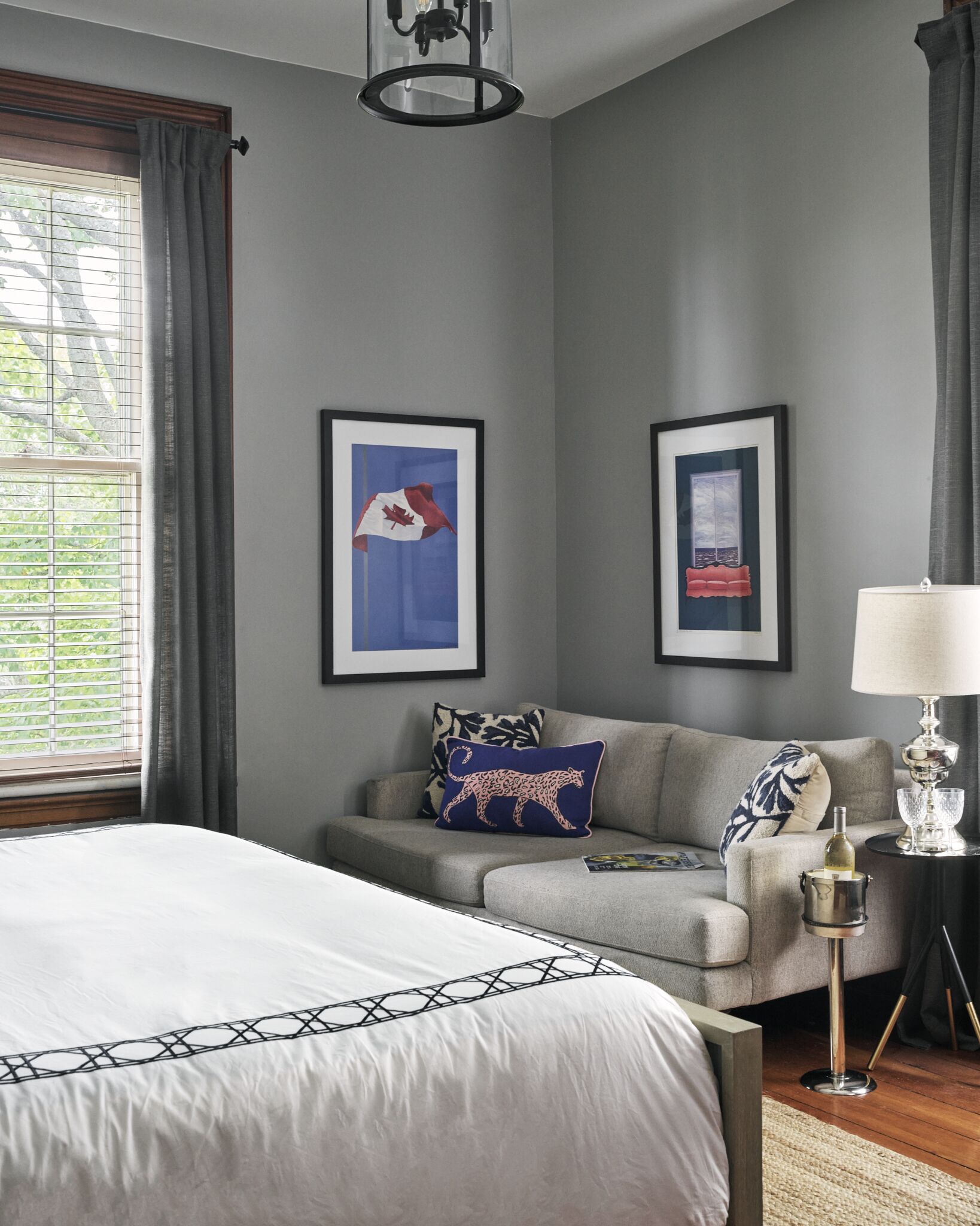 A bedroom with a bed, a sofa, a lamp, and two framed pictures on the wall.