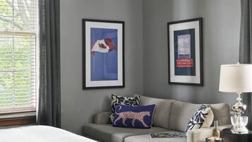 A bedroom with a bed, a sofa, a lamp, and two framed pictures on the wall.