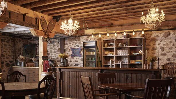 A rustic bar area with wooden furniture, a stone wall, and a Miller High Life sign. - The Eddie Hotel and Farm (Prince Edward)