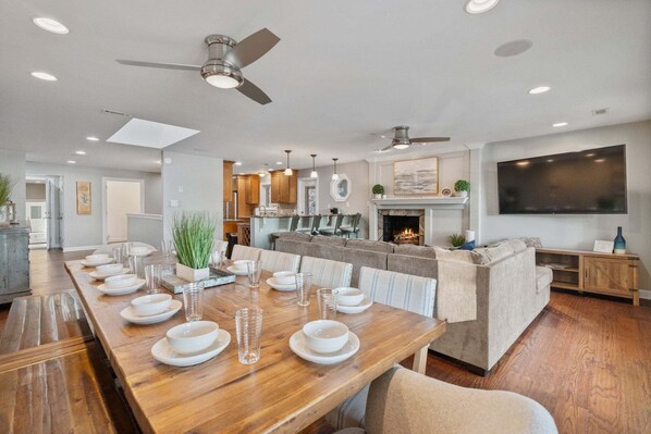 A modern dining area with a wooden table set for six, a sofa, and a TV mounted on the wall.