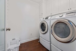 A laundry room with two front-loading washing machines, a white door, and a white laundry basket.