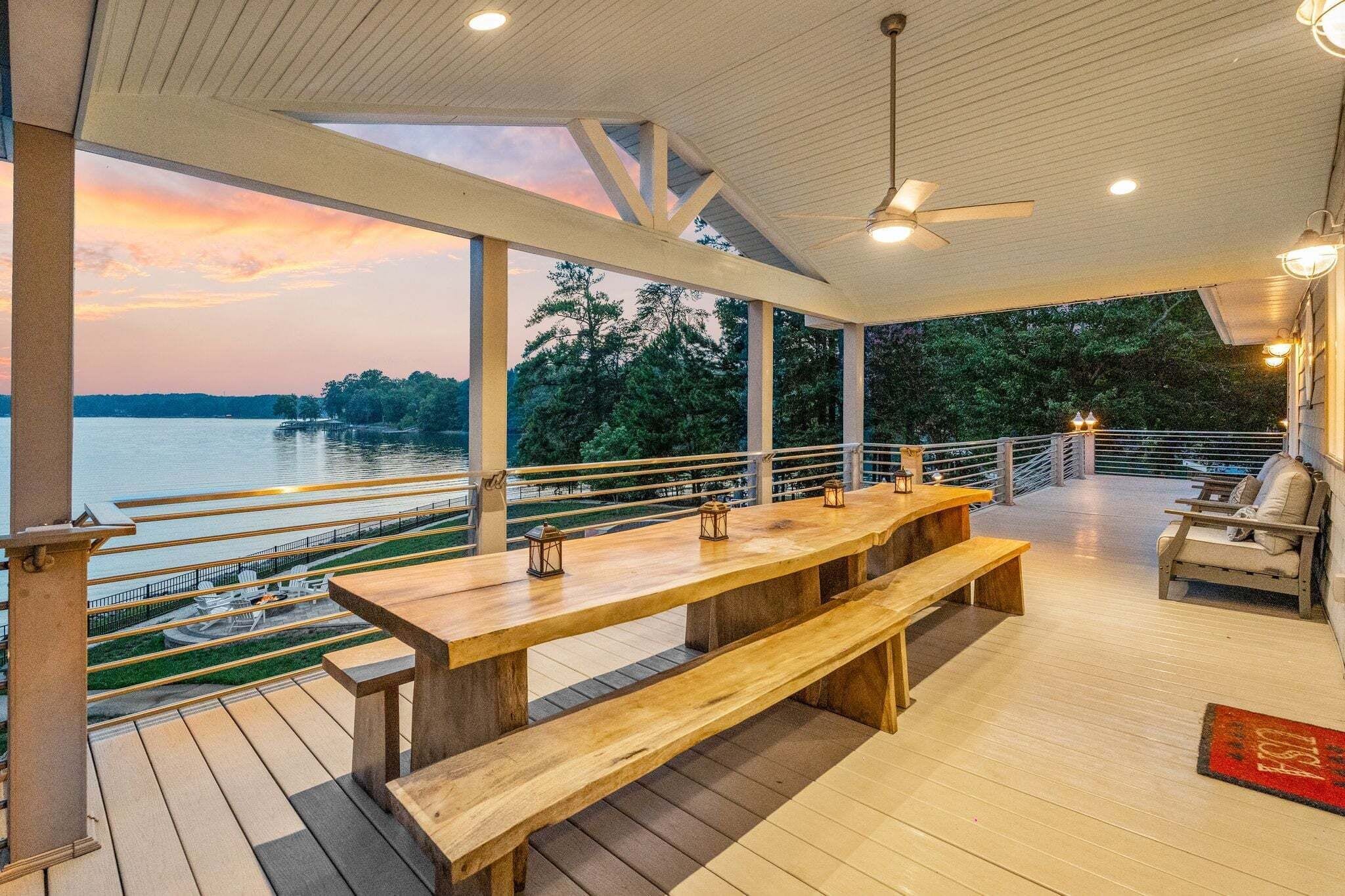 An outdoor deck with a wooden table and benches, overlooking a body of water and trees.