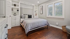 Een slaapkamer met een bed, inbouwplanken, een plafondventilator en een raam met zonwering.