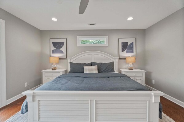 A bedroom with a bed, two bedside tables, two lamps, and two framed pictures on the walls.