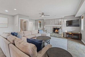 A living room with a sectional sofa, a fireplace, a flat-screen TV, and a ceiling fan. - Casa Sul Lago by SoCharm | Lakefront Retreat |Pool| Dock (Troutman)