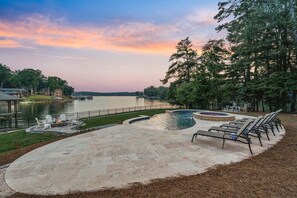 A pool area with lounge chairs, a fire pit, and a view of a lake.