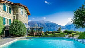 Un bâtiment en pierre doté d’une piscine, d’une véranda en verre et offrant une vue sur la montagne.