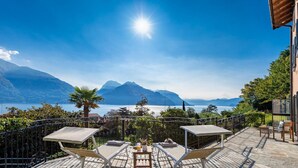 Une terrasse avec des chaises longues et une table, offrant une vue sur un lac et des montagnes.