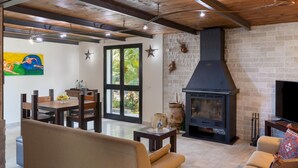 Un salon chaleureux avec une cheminée, des meubles en bois et une grande fenêtre donnant sur un paysage verdoyant.