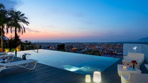 Une piscine à débordement située sur le toit, avec des chaises longues et une vue sur la ville au crépuscule.
