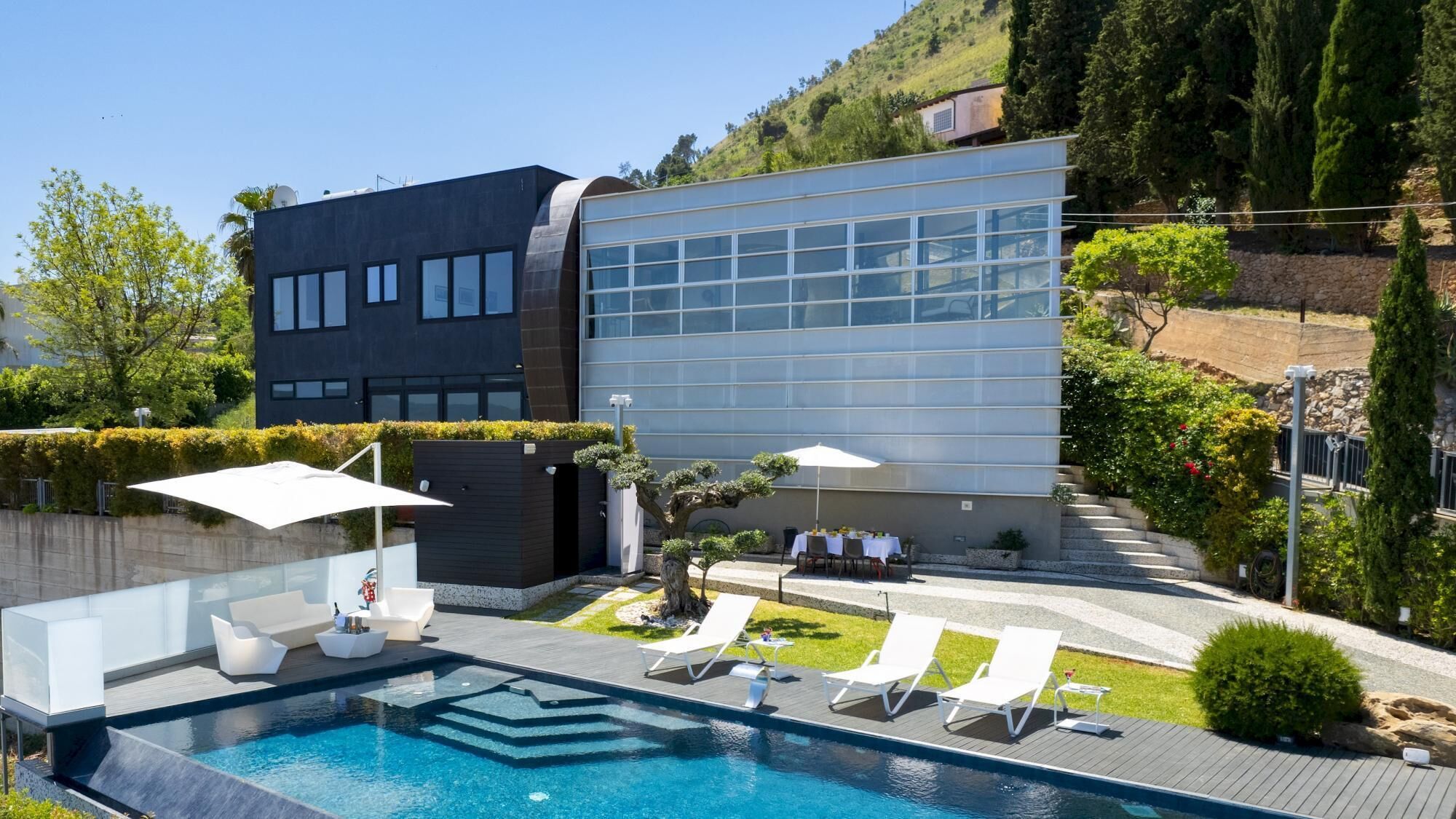 Ein modernes Gebäude mit Pool, Sitzgelegenheiten im Freien und einem angelegten Garten.