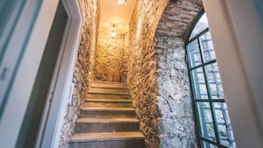 A stone staircase with a wooden door at the top, leading to a room with a large window.