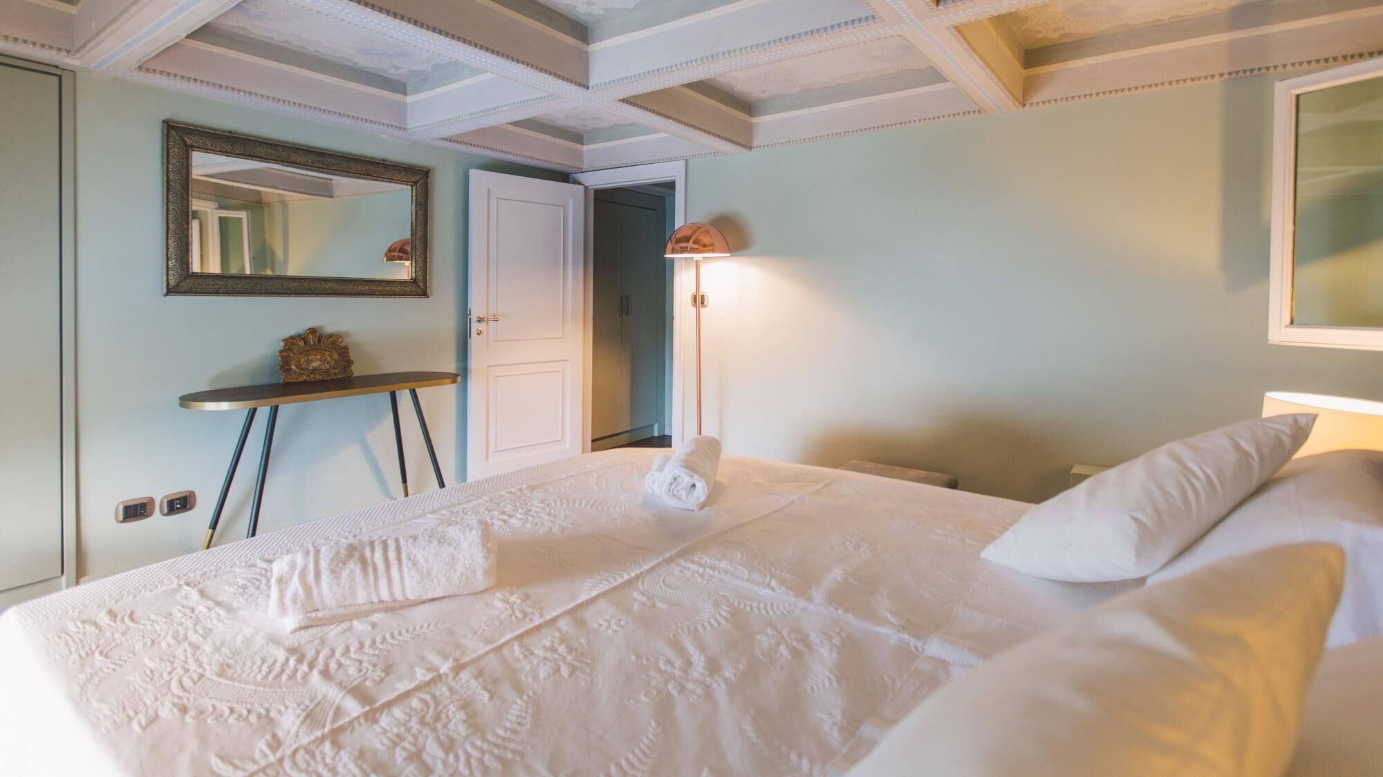 A hotel room with a large bed, a bedside table, a lamp, and a mirror on the wall.