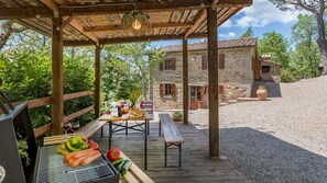 A wooden deck with a grill, picnic table, and outdoor dining setup. - Casa Largnano 6 2 in Arezzo (Castiglion Fiorentino)
