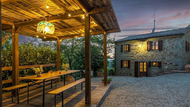 A stone building with wooden benches and a covered patio area with string lights. - Casa Largnano 6 2 in Arezzo (Castiglion Fiorentino)
