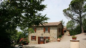 A stone house with a gravel driveway, wooden shutters, and potted plants. - Casa Largnano 6 2 in Arezzo (Castiglion Fiorentino)