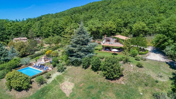 Una propiedad en una ladera con piscina, una casa de piedra y abundante vegetación.