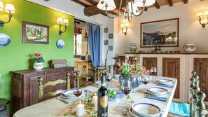 Uma sala de jantar com uma mesa comprida posta para refeição, cadeiras de madeira e uma parede verde com obras de arte.