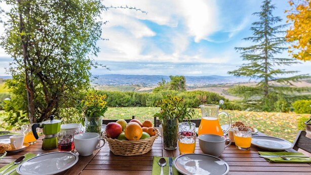 A breakfast table set outdoors with a scenic view, including fruits, beverages, and a pitcher. - Villa Mila 6 in Gualdo Cattaneo (Gualdo Cattaneo)