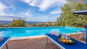 A swimming pool with a view of the countryside, a lounge chair with a towel, and a tray with fruits and a pitcher. - Villa Mila 6 in Gualdo Cattaneo (Gualdo Cattaneo)
