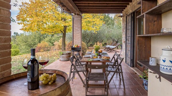Une terrasse extérieure avec une table dressée pour le petit-déjeuner, un barbecue et une vue sur le feuillage automnal.