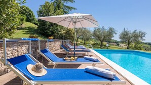A poolside area with lounge chairs, a sun umbrella, and a view of the surrounding landscape. - Villa Mila 6 in Gualdo Cattaneo (Gualdo Cattaneo)